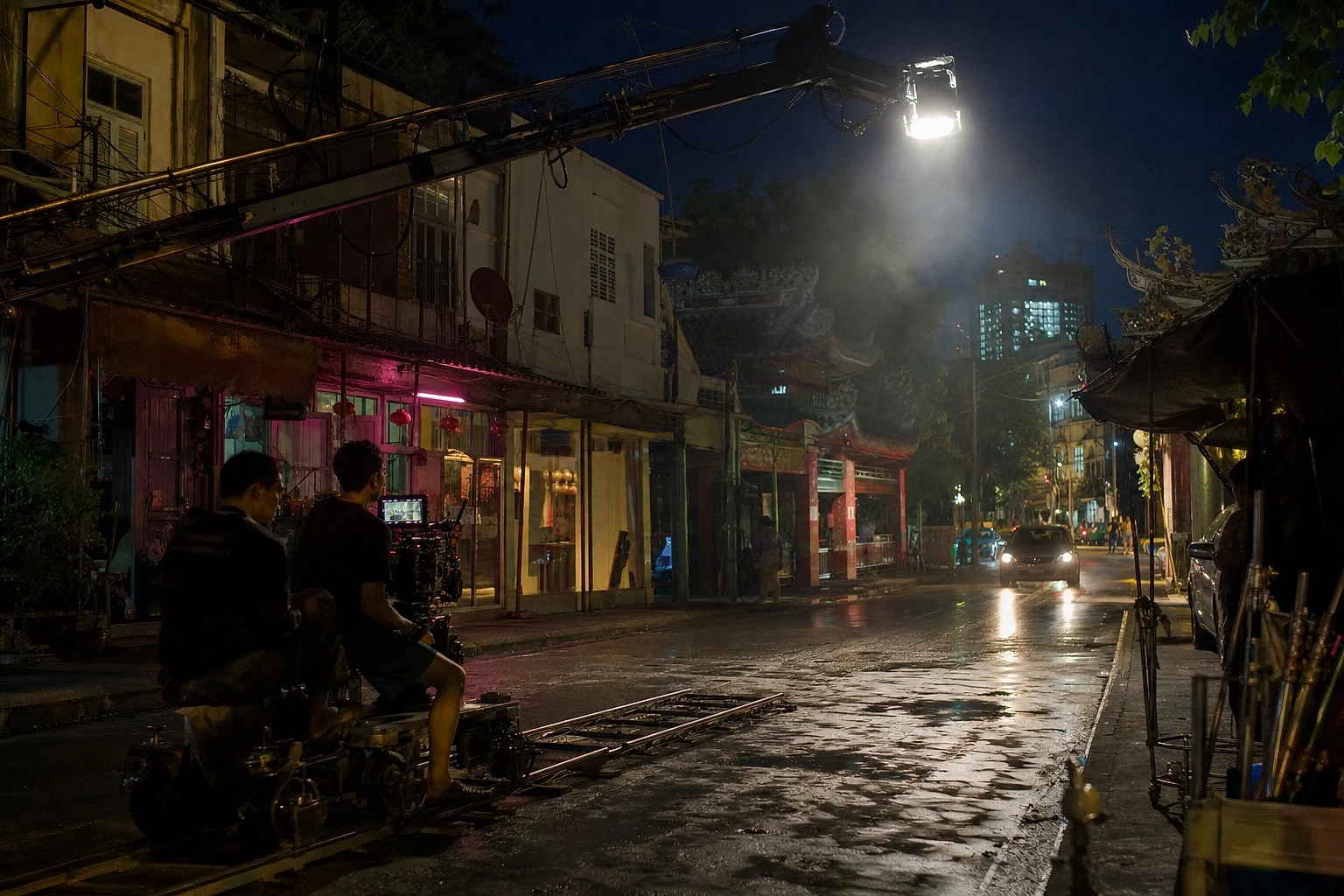 A night shoot on a Bangkok street: dolly and camera in the foreground, a jib light overhead, the lit street beyond